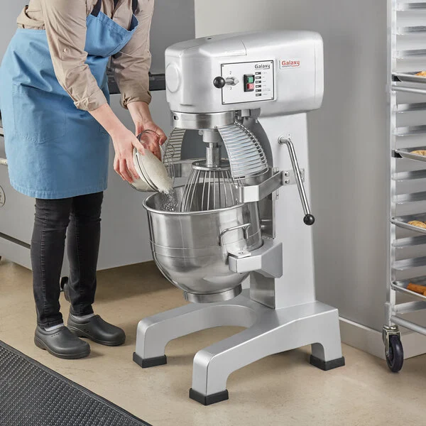 A woman pouring the flour into a commercial flour bakery mixer